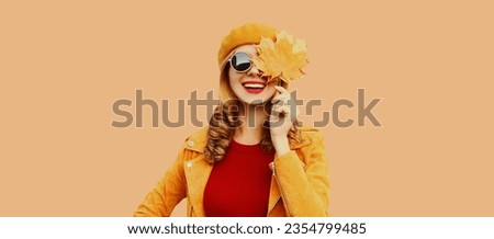Autumn color style outfit, portrait of beautiful smiling young woman with yellow maple leaves wearing orange french beret hat, jacket on brown studio background