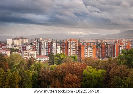 Autumn colors of foreground trees, doft light on old buildings and dramatic, blue hour sky above Pirot cityscape