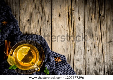 Autumn comfort and warm concept. Tea glass cup with lemon, mint and spices, on old rustic wooden background with warm blankets. Copy space for text