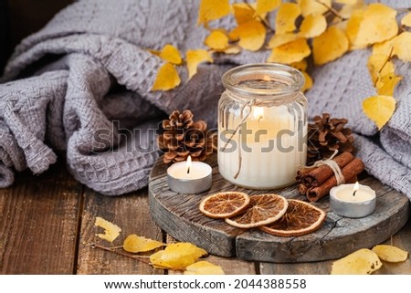 Autumn composition with aromatic candle, dry citrus, cinnamon. Aromatherapy on a grey fall morning, atmosphere of cosiness and relax. Wooden background close up