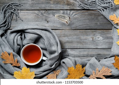 Autumn Composition, Fall Leaves, Hot Steaming Cup Of Tea And A Warm Scarf On Wooden Table Background.