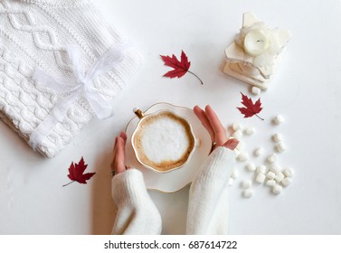 Autumn composition. Hot chocolate, knitted blanket, lit candle, autumn leaves. Flat lay, top view, white background. Hands holding cup of warm drink