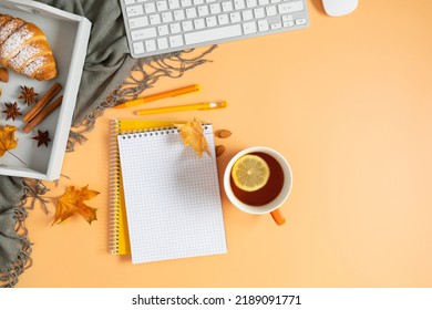 Autumn Composition. Office Desk With Cup Of Hot Tea With Lemon, Empty Notebook, Keyboard, Scarf, Dry Leaves On Isolated Beige Background. Autumn, Fall Business Concept. Flat Lay, Top View, Copy Space