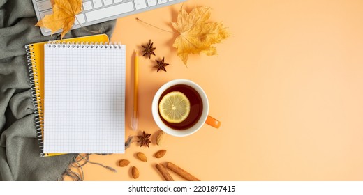 Autumn Composition. Office Desk With Cup Of Hot Tea With Lemon, Empty Notebook, Keyboard, Scarf, Dry Leaves On Isolated Beige Background. Autumn, Fall Business Concept. Flat Lay, Top View, Copy Space