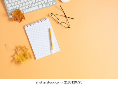 Autumn Composition. Office Desk With Empty Notebook, Keyboard, Scarf, Dry Leaves On Isolated Beige Background. Autumn, Fall Business Concept. Flat Lay, Top View, Copy Space