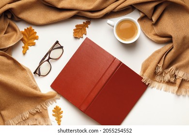 Autumn composition. Open inverted book glasses cashmere scarf, coffee cup with autumn leaves on a white background. Flat lay top view