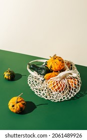 Autumn Composition With Pumpkins And Gourdes In White Crochet Shopping Bag Against Green And Beige Two Tone Background. Creative Vegetable Fall Food Concept. Minimal Thanksgiving Still Live Idea.