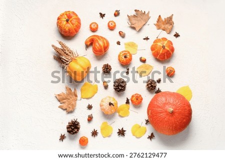 Autumn composition with ripe pumpkins, pine cones, spices and fallen leaves on light background