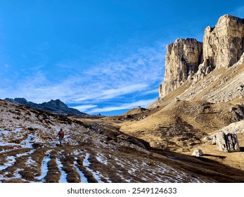 An autumn day near Passo Giau, Dolomites, where a lone hiker walks through the prehistoric rocky valley. The sun casts a golden glow over the landscape, with blue skies and distant peaks... - Powered by Shutterstock