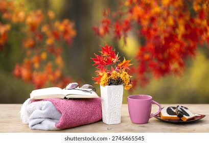 Autumn decor. Fall background. Soft autumn light creates a cozy and comforting scene outdoors. A cup of coffee and book under autumn fall leaves. Cozy autumnal feeling. Cozy autumn day for resting.