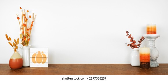 Autumn decor on a wood shelf against a white wall banner background. Pumpkin sign, candles and vases with fall colors.  - Shutterstock ID 2197388257