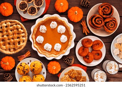 Autumn desserts table scene with an assortment of traditional fall sweet treats. Above view over a rustic wood background. Pumpkin and apple pies, apple cider donuts, muffins, cookies, tarts.