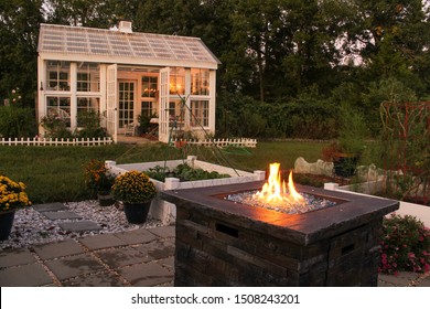 Autumn evening in a beautiful garden with a fire lit raised beds and a white Victorian style greenhouse with a cupola and weather vane in background 