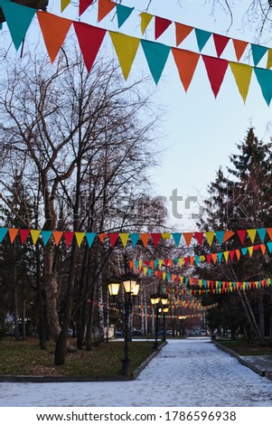 Autumn evening in a city park. The first snow is on the sidewalk. The alley is decorated with garlands of color flags.