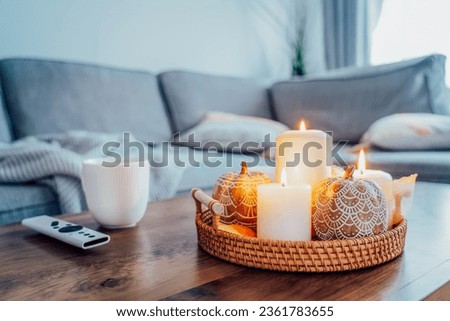Autumn fall cozy mood composition for hygge home decor. Orange pumpkins, burning candles, cup with hot drink and remote controller on coffee table in living room. Movie night at home. Cozy relax time.
