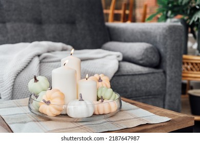 Autumn, Fall Cozy Mood Decor Composition For Hygge Home. Decorative Pumpkins And White Burning Candles On The Glass Tray On The Coffee Table In The Living Room With Sofa. Selective Focus.