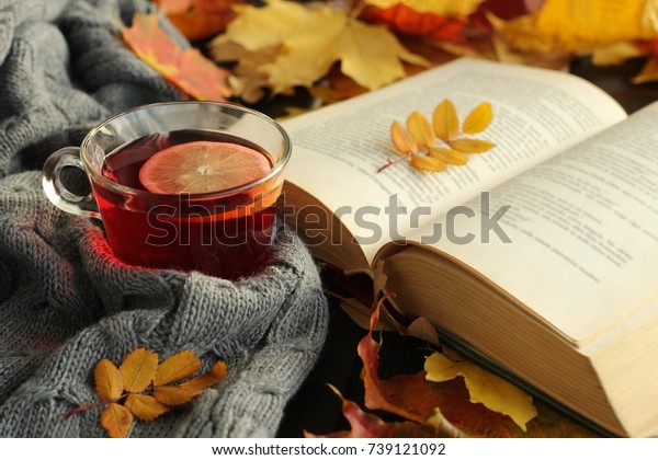 Autumn, fall  leaves, cup\
of tea, opened book  and warm scarf on wooden table. Seasonal, book\
reading, Sunday relaxing, teatime and still life concept. Selective\
focus.