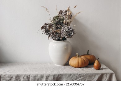 Autumn, Fall Still Life. Big Ceramic Vase With Dry Hydrangea Flowers, Grass Boho Bouquet. Orange Pumpkins And Pear Fruit On Linen Table Cloth. White Wall Background. Halloween, Thanksgiving Holiday.