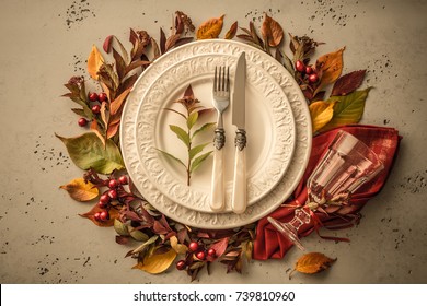 Autumn (fall) Or Thanksgiving Table Setting Design Captured From Above (top View, Flat Lay). White Plate, Glass, Cutlery And Decorations (colorful Leaves). Dark Moody Light.