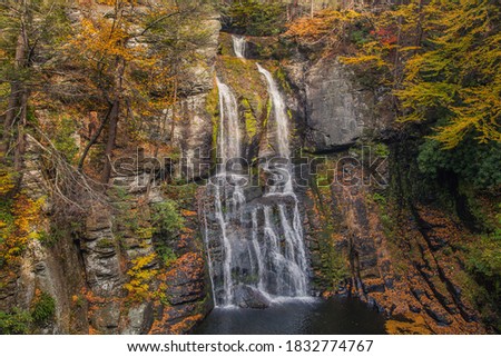 Autumn, fall waterfall surrounded trees with yellow, orange and green leaves, foliage. Rocks and mountain covered with golden leaves. Bushkill falls.