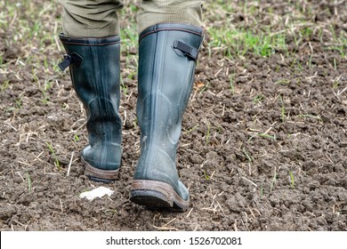 In autumn, a farmer goes with his green rubber boots over the freshly sown field.
