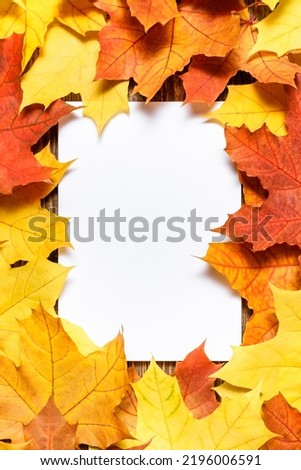 Autumn festive card template. Blank white paper mockup with fallen autumn dried leaves on wooden table background. Colorful, variegated foliage. Flat lay, top view, copy space