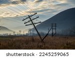 Autumn field with fallen electric poles at dawn. The wires were stretched dangerously under the weight of the support. Dramatic skies heighten the atmosphere of decadence