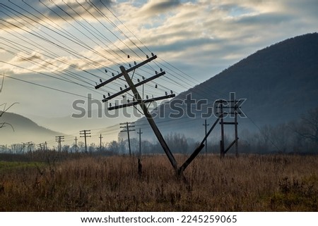 Autumn field with fallen electric poles at dawn. The wires were stretched dangerously under the weight of the support. Dramatic skies heighten the atmosphere of decadence
