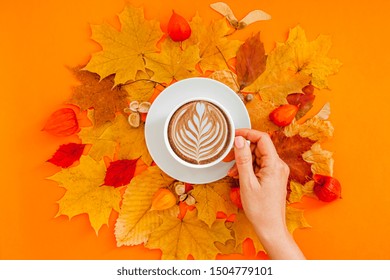 Autumn flat lay composition with dry leaves wreath frame and coffee latte cup in woman hand on bold orange color background. Creative autumn thanksgiving, fall, halloween concept. Top view, copy space - Powered by Shutterstock