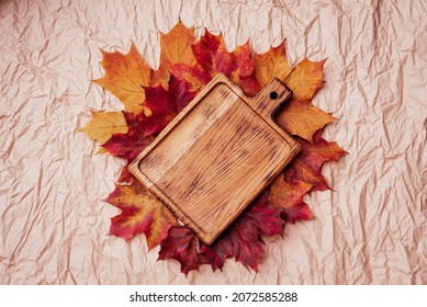 Autumn flat lay composition. Empty wooden plate cutting board and autumn leaves on paper background top view mock up. copy space. Fall season. golden maple leaves.