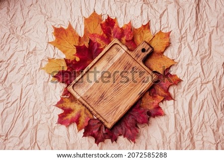 Autumn flat lay composition. Empty wooden plate cutting board and autumn leaves on paper background top view mock up. copy space. Fall season. golden maple leaves.