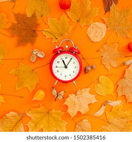 Autumn flat lay composition with red alarm clock and dry leaves on bold orange color background. Creative autumn, thanksgiving, fall, halloween concept. Top view, copy space