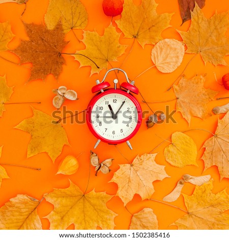 Autumn flat lay composition with red alarm clock and dry leaves on bold orange color background. Creative autumn, thanksgiving, fall, halloween concept. Top view, copy space