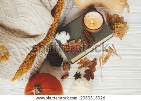 Autumn flat lay. Pumpkin, cozy sweaters, autumn leaves, burning candle and vintage book on white wooden background in room. Hello autumn, cozy slow living.  Happy Thanksgiving