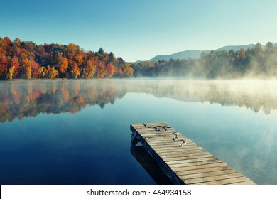Autumn foliage and fog lake in morning with boat dock