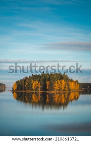 Autumn forest on a small island coloured in autumn colours. Reflection of orange and green trees in the lake around the town of Sotkamo, Kainuu, Finland. Breathtaking beauty created by mother nature.