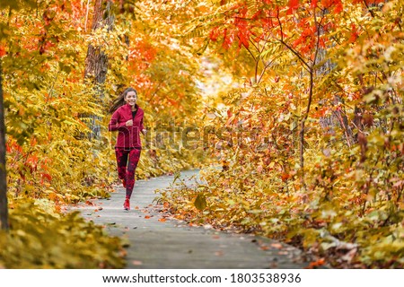 Autumn forest run path. Fall trail runner woman running in beautiful foliage woods nature background. Asian happy sports woman training outdoor. 