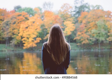 Autumn girl standing backwards and watching nature. Autumn forest colors with girl back view. Outdoor autumn landscape. Orange autumn portrait. Orange tranquility - woman watching woods outdoor