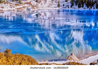 Autumn gives way to winter, air temperature drops and the water in the lake begins to freeze. Texture and patterns of ice on the serene water surface of mountain lake; Big Almaty lake in Kazakhstan