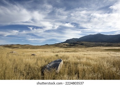 Autumn gold dry grasses, big sky and clouds, rock, and mountains landscape along Old Yellowstone Trail in Gardiner, Montana