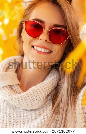 Autumn happiness portrait of a beautiful young woman with a smile and red sunglasses wearing a fashionable knitted sweater in the colorful leaves walks in the fall park 