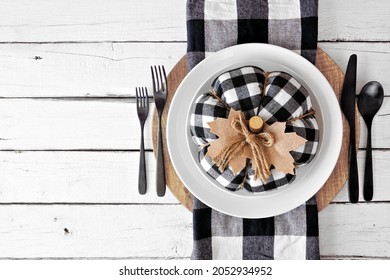Autumn harvest or thanksgiving dinner table setting with buffalo plaid pumpkin and napkin, plates and flatware. Overhead view on a white wood background.