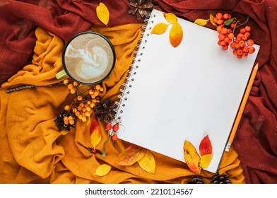 Autumn home cozy composition with yellow and burgundy blankets, cup of coffee, red and yellow leaves and notebook with copy space. Fall season template for feminine blog social media.