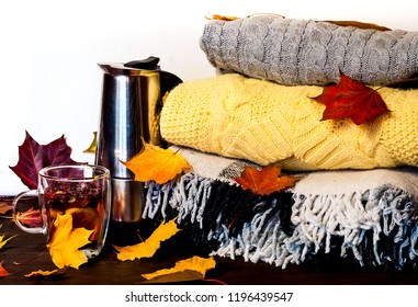 Autumn Home Decor.Metal Coffee Pot And Glass Cup  With Healing Tea And Cinnamon Sticks Amid Bright Yellow Leaves On The Background Of Knitted Clothes And Checkered Plaid. Hygge Style