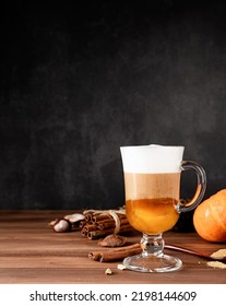 Autumn hot drinks. Pumpkin spice latte in a glass mug with cinnamon and ginger on dark background with copy space