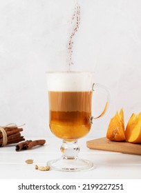 Autumn Hot Drinks. Pumpkin Spice Latte In A Glass Mug With Cinnamon On Light Background With Copy Space. Cinnamon Powder Falling