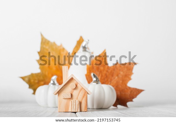 Autumn house insurance, sale, rent concept. White\
decorative pumpkins and autumn yellow leaves with miniature wooden\
house close-up and copy\
space..