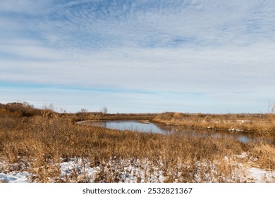 Autumn landscape. Cold, blue sky above the horizon. Sunny day. First, white snow melts on a field with dry grass. There is a lake in the background. - Powered by Shutterstock