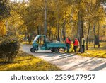 Autumn landscape with maintenance crew at work. Groundskeepers preparing park for changing seasons. Municipal workers in uniform take care of the lush autumn park