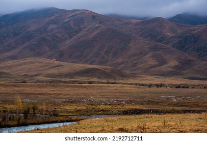 Autumn Landscape Of A Rainy Day In The Altai Mountains, Russia. Travel To Distant Beautiful Places Of The Planet. Scenic View Of Hills With Yellow Trees And Fog On Mountain Tops In The Background.